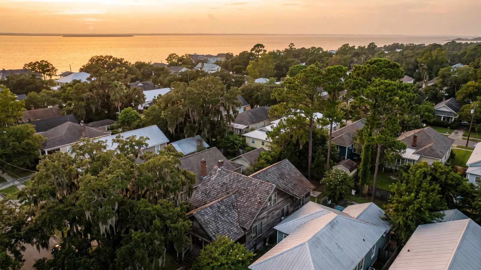 Rooftops of a Mobile neighborhood at sunset with live oaks and Mobile Bay on the horizon